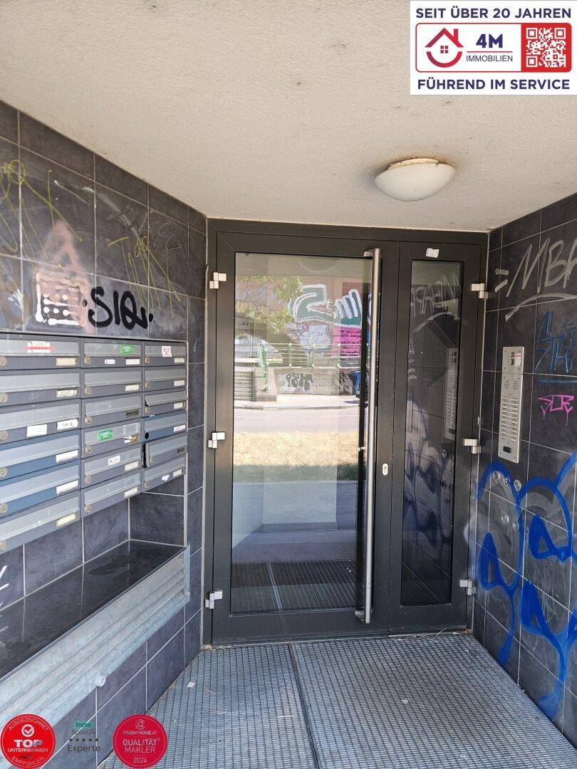 Eingangsbereich des Gebäudes mit Briefkästen und Gegensprechanlage, umgeben von Fliesen.