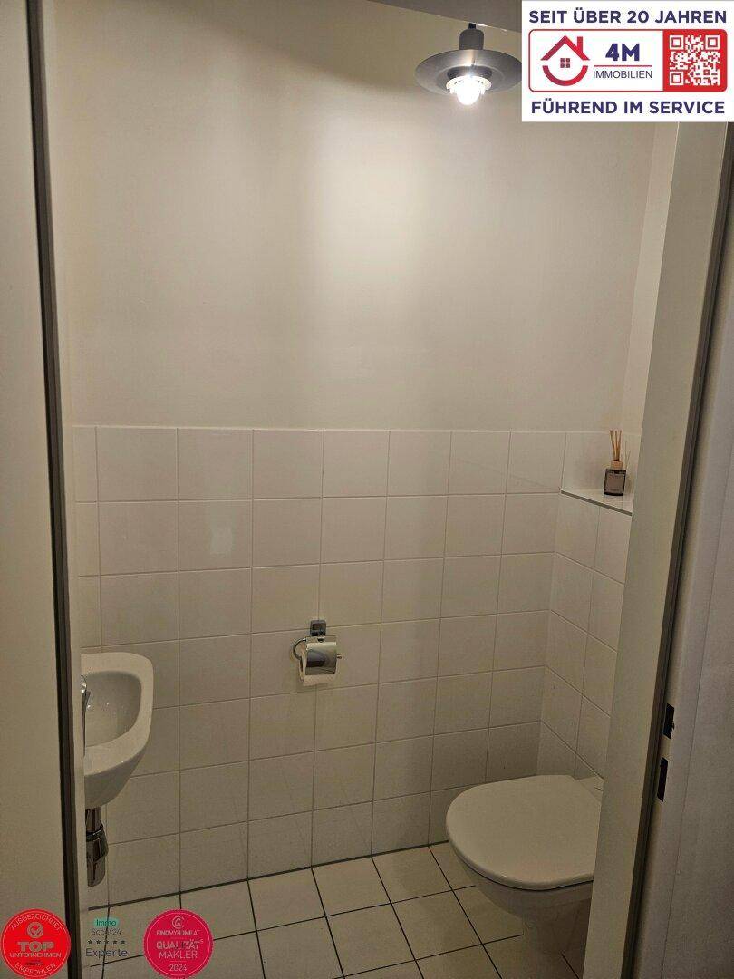 Separate Gästetoilette mit WC, kleinem Waschbecken und weißen Wandfliesen.