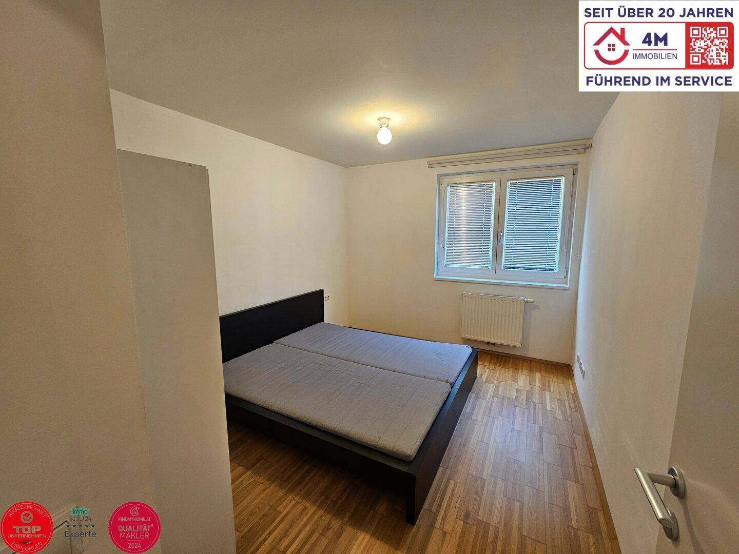 Schlafzimmer mit Doppelbett, Parkettboden und Fenster, das für natürliches Licht sorgt.