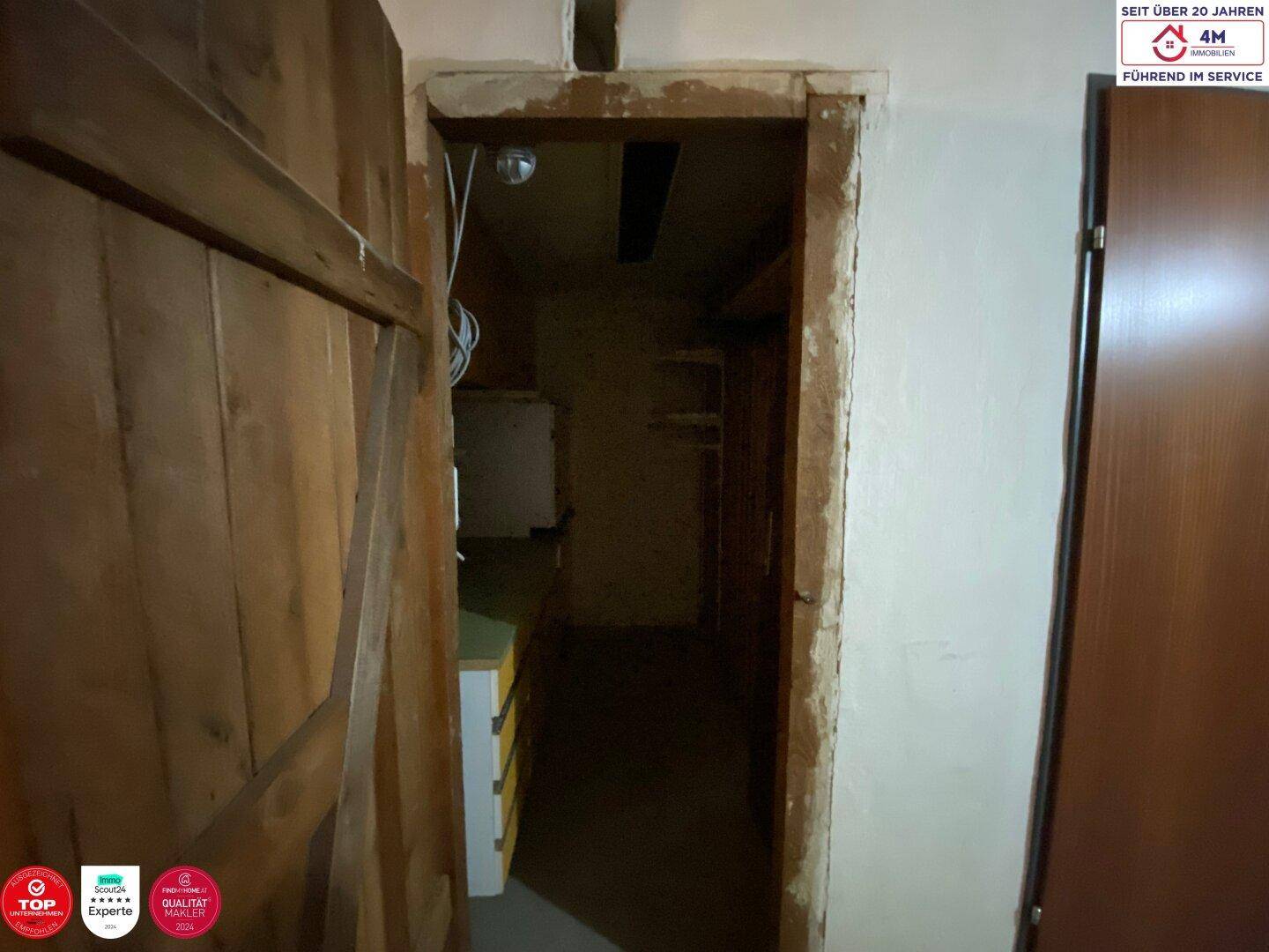 Dunkler, unklarer Raum, möglicherweise ein Abstellraum oder Kellerbereich, mit Holztür.