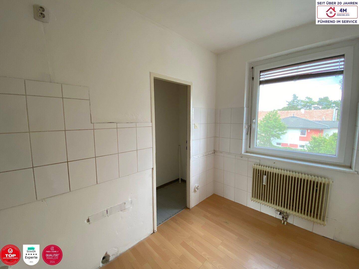 Leere Küche mit Fliesen an den Wänden, Laminatboden und einem Fenster mit Blick ins Grüne.