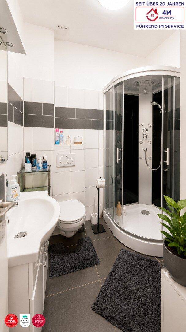 Modernes Badezimmer mit Duschkabine, WC und Waschbecken in hellen und dunklen Fliesen.