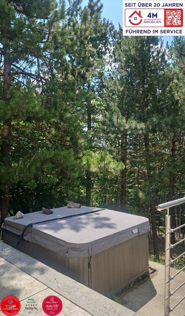 Außenbereich mit Whirlpool auf einer Terrasse, umgeben von hohen Bäumen.