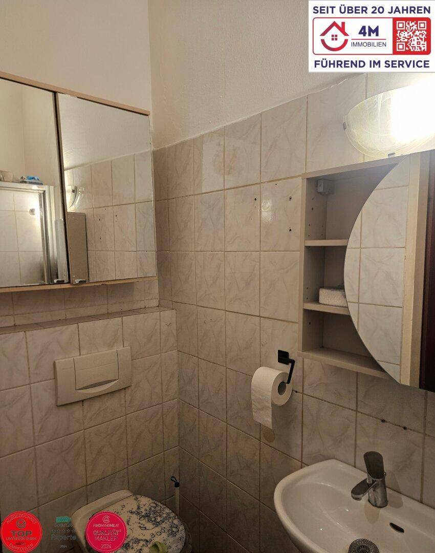 Gefliestes Badezimmer mit Toilette, Waschbecken und Spiegelschrank.