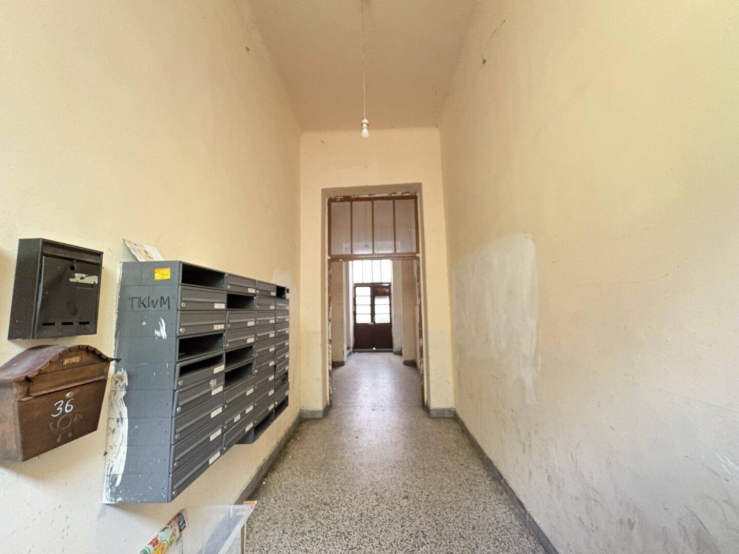 Langer, schmaler Flur im Eingangsbereich eines Mehrfamilienhauses mit Briefkästen.