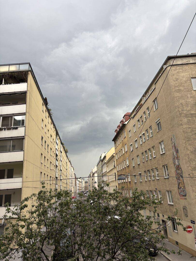 Blick auf eine städtische Straße zwischen hohen Gebäuden unter einem bewölkten Himmel.