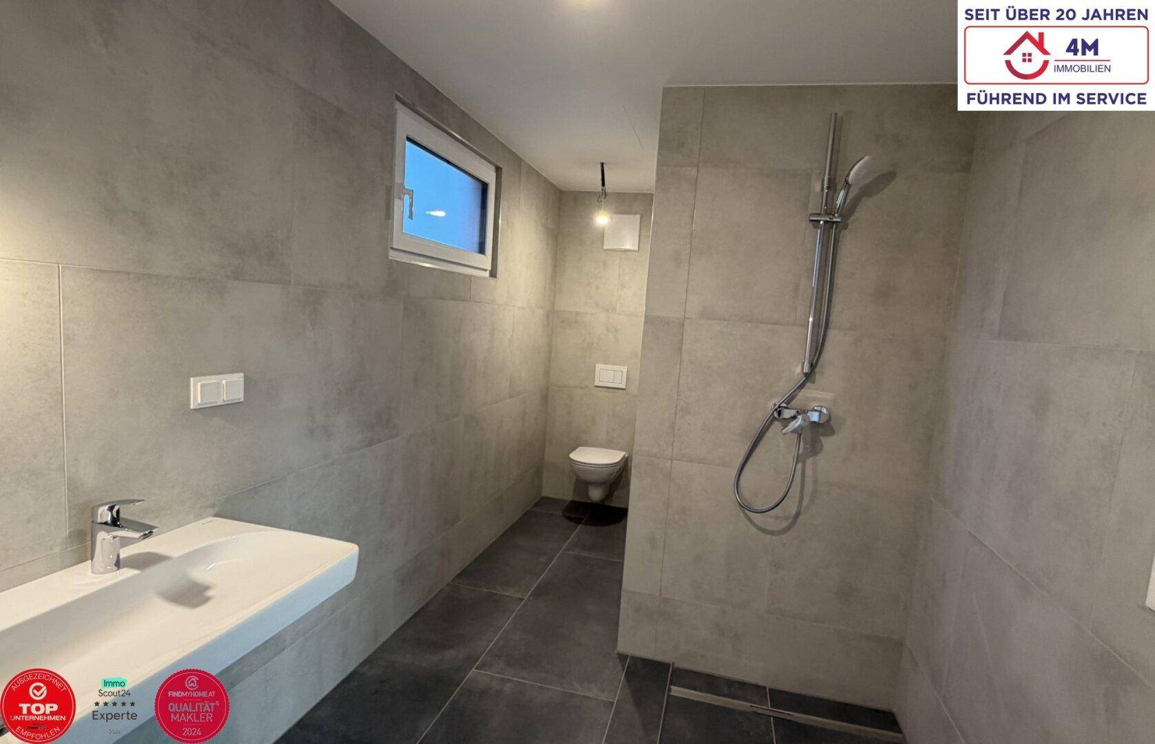 Modernes Badezimmer mit ebenerdiger Dusche, Wand-WC und Fenster für natürliche Belüftung.