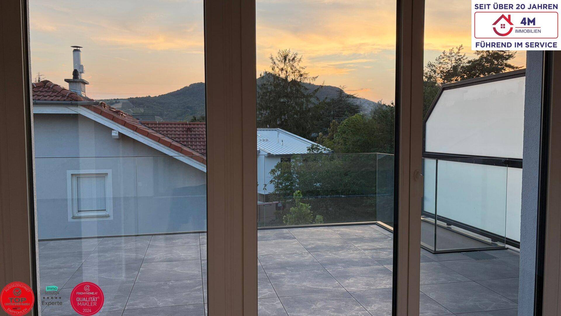 Blick von innen auf die großzügige Terrasse mit Glasgeländer und weitem Ausblick.