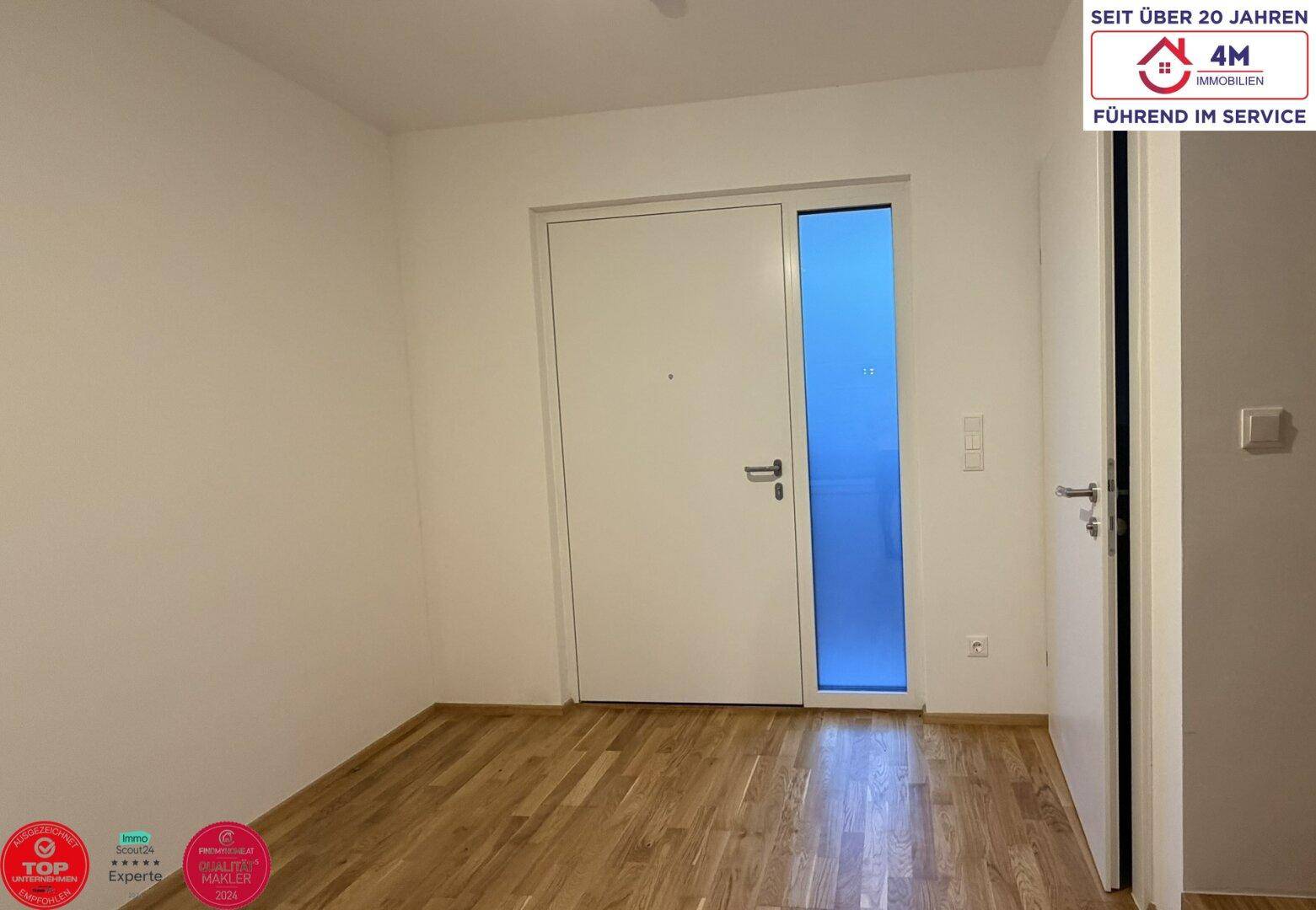 Heller Eingangsbereich mit Parkettboden und moderner Haustür, empfängt Bewohner und Gäste.