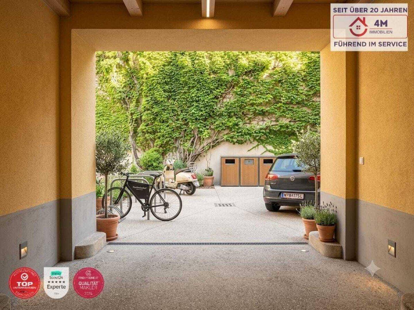 Eingangsbereich zu einem begrünten Innenhof mit Parkmöglichkeiten und Fahrrädern.