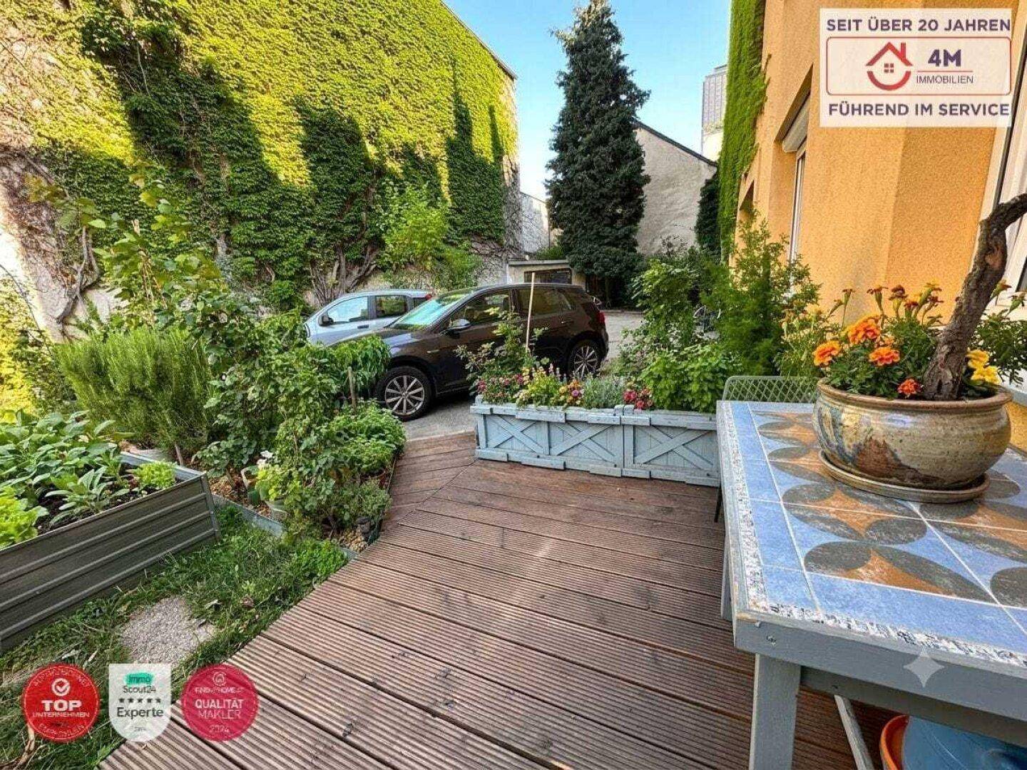 Holzterrasse mit Gartentisch und Pflanzen, umgeben von begrünten Wänden.