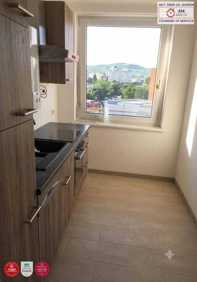 Funktionale Küche mit Holzschränken, dunkler Arbeitsplatte und Fenster mit Ausblick.
