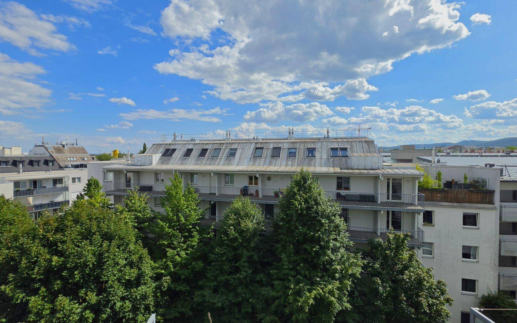 Mehrfamilienhaus mit Mansarddach und vielen Dachfenstern, umgeben von Bäumen.