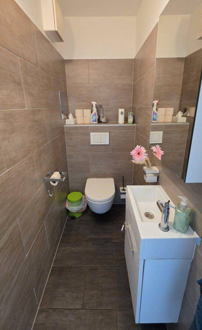 Modern gefliestes Gäste-WC mit Wand-WC und kleinem Waschbecken.