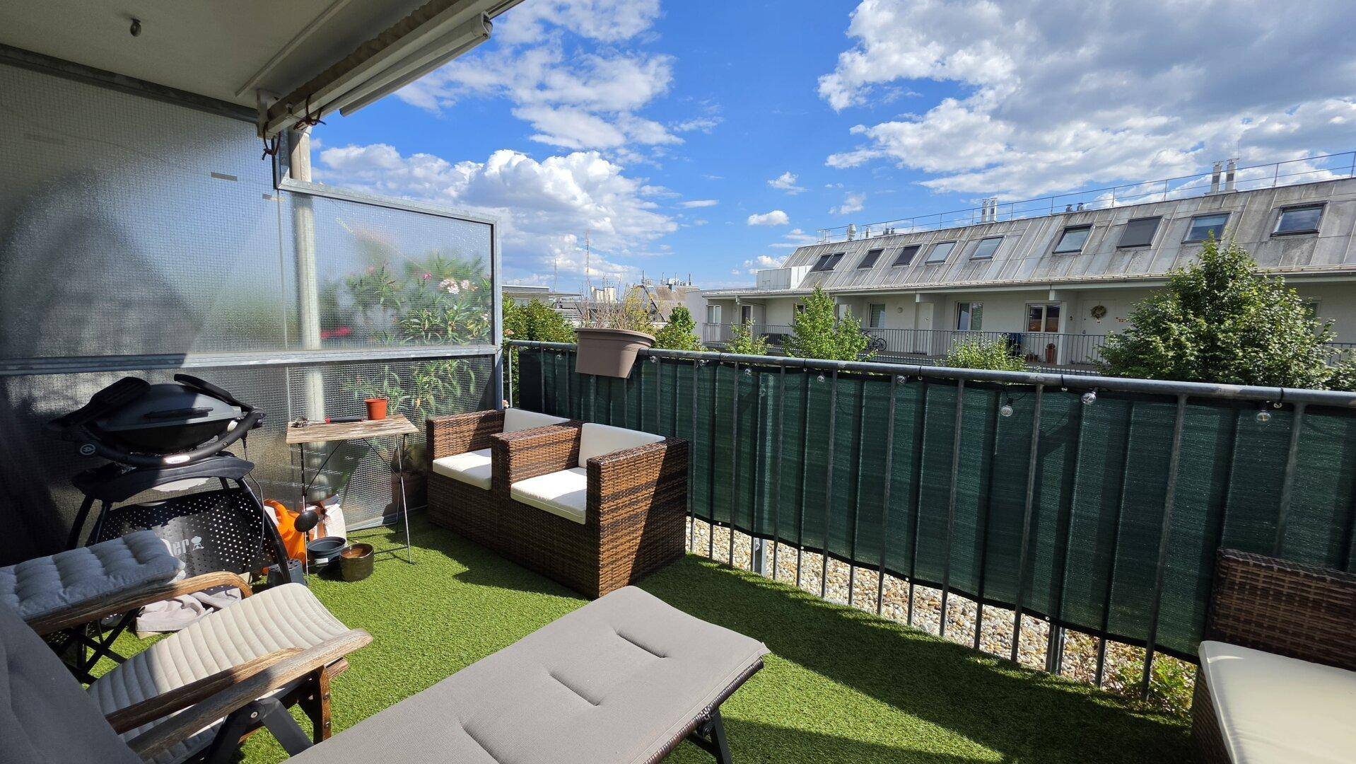 Gemütlicher Balkon mit Kunstrasen, Gartenmöbeln und Blick auf die Umgebung.