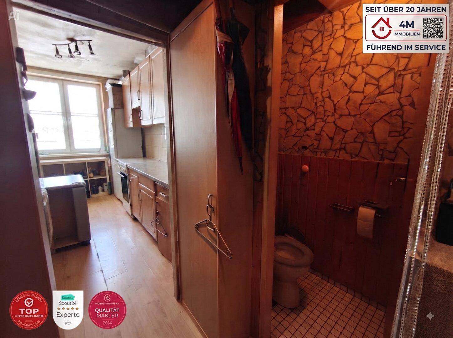 Schmale Küche mit Holzschränken, Fliesenboden und angrenzender kleiner Toilette.