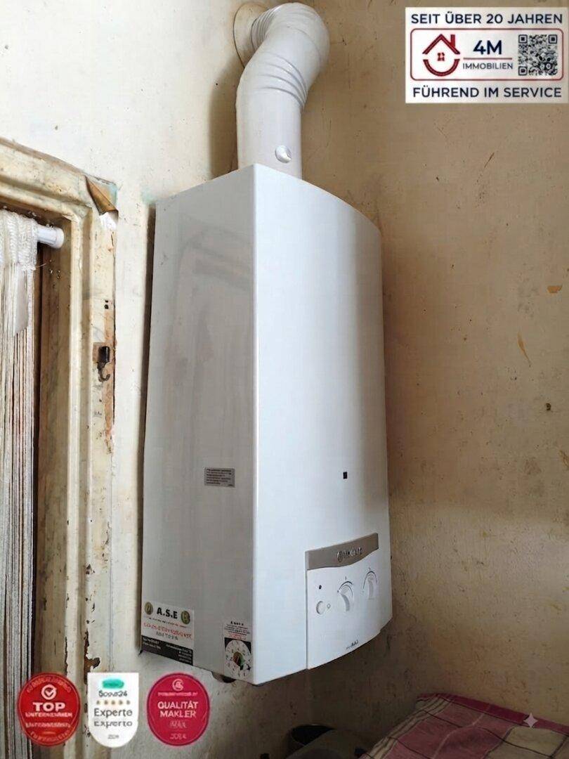Wandmontierter Warmwasserbereiter in einem kleinen Raum, wahrscheinlich ein Hauswirtschaftsraum.