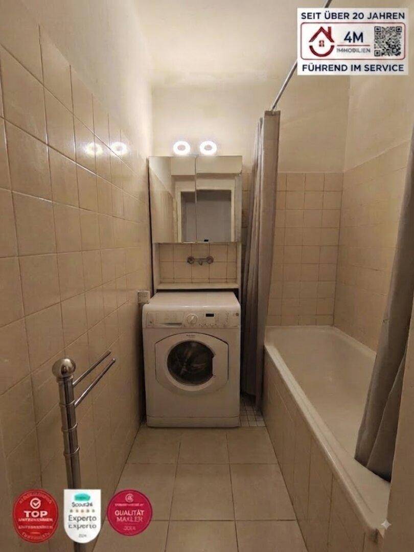 Kleines Badezimmer mit Badewanne, Waschmaschine und beigefarbenen Fliesen an den Wänden.