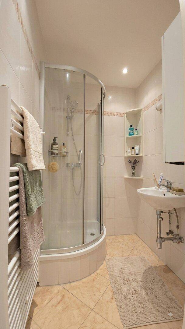 Helles Badezimmer mit Duschkabine, Waschbecken und beheiztem Handtuchhalter.