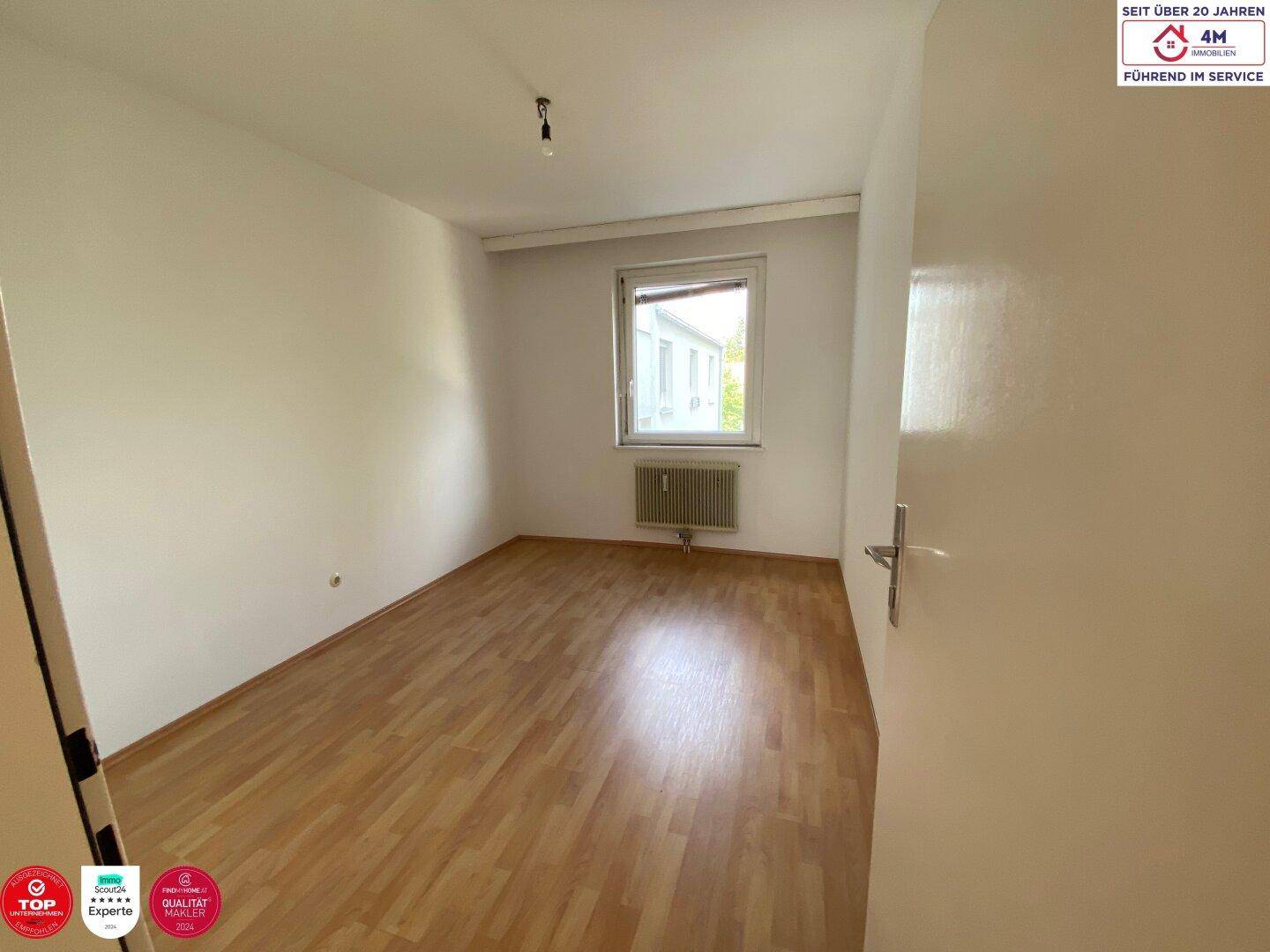 Leeres Schlafzimmer mit Laminatboden und einem Fenster, das den Raum gut belichtet.