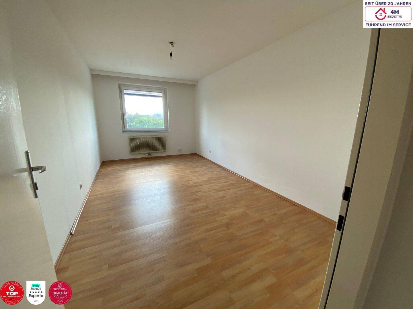 Geräumiges, leeres Zimmer mit Laminatboden und einem Fenster, das den Raum erhellt.