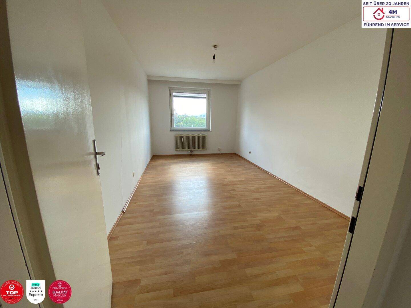 Leeres Zimmer mit Laminatboden und einem Fenster, das für ausreichend Helligkeit sorgt.