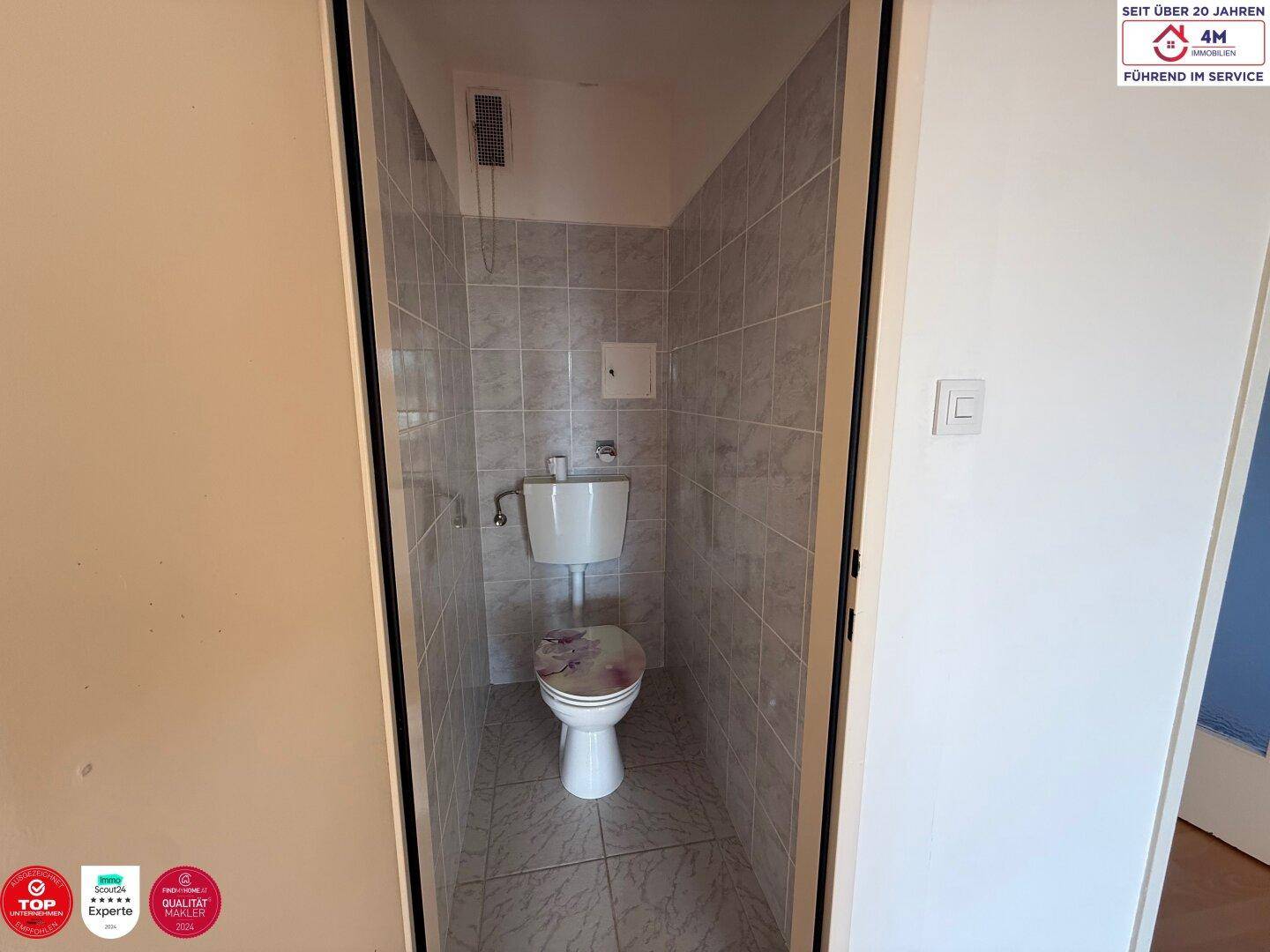 Separate Toilette mit Fliesen an den Wänden und auf dem Boden, in einem kleinen Raum.