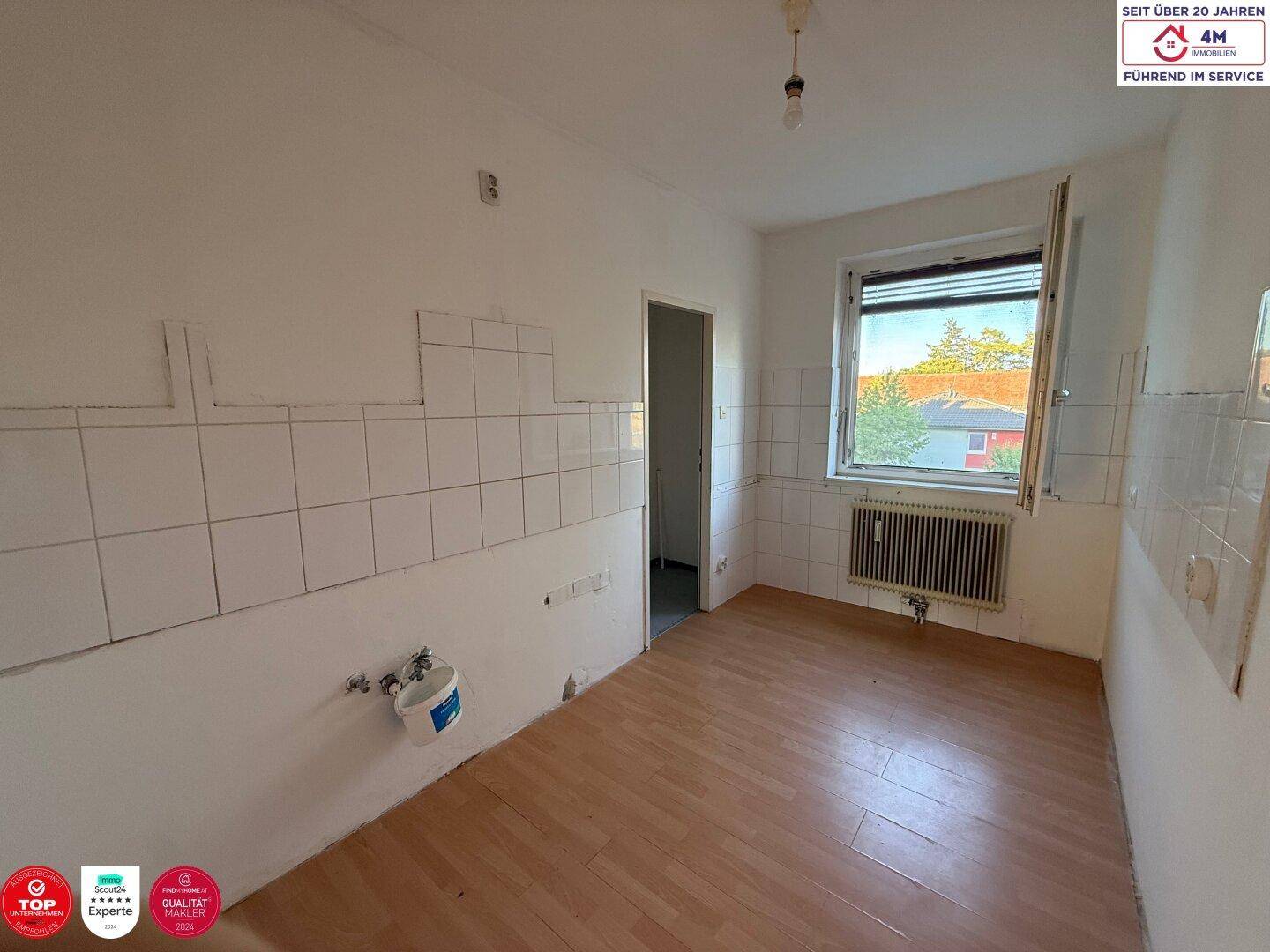 Leere Küche mit Wandfliesen, Laminatboden und einem Fenster mit Blick ins Grüne.