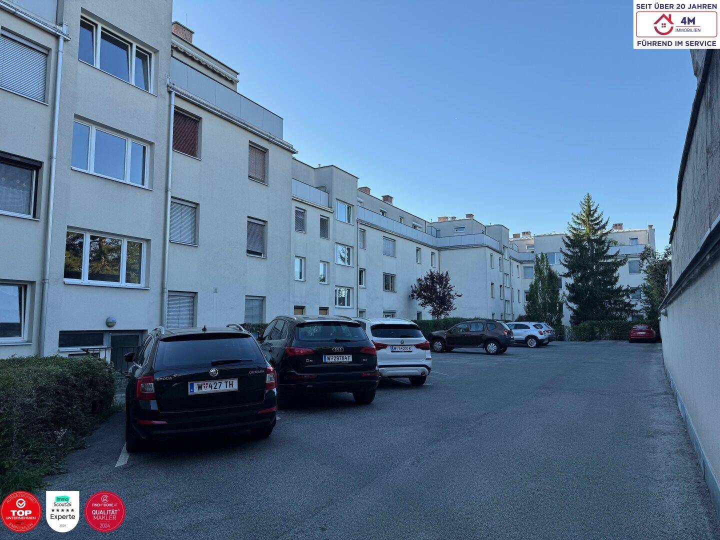 Rückansicht eines Mehrfamilienhauses mit Parkplätzen und grüner Umgebung.