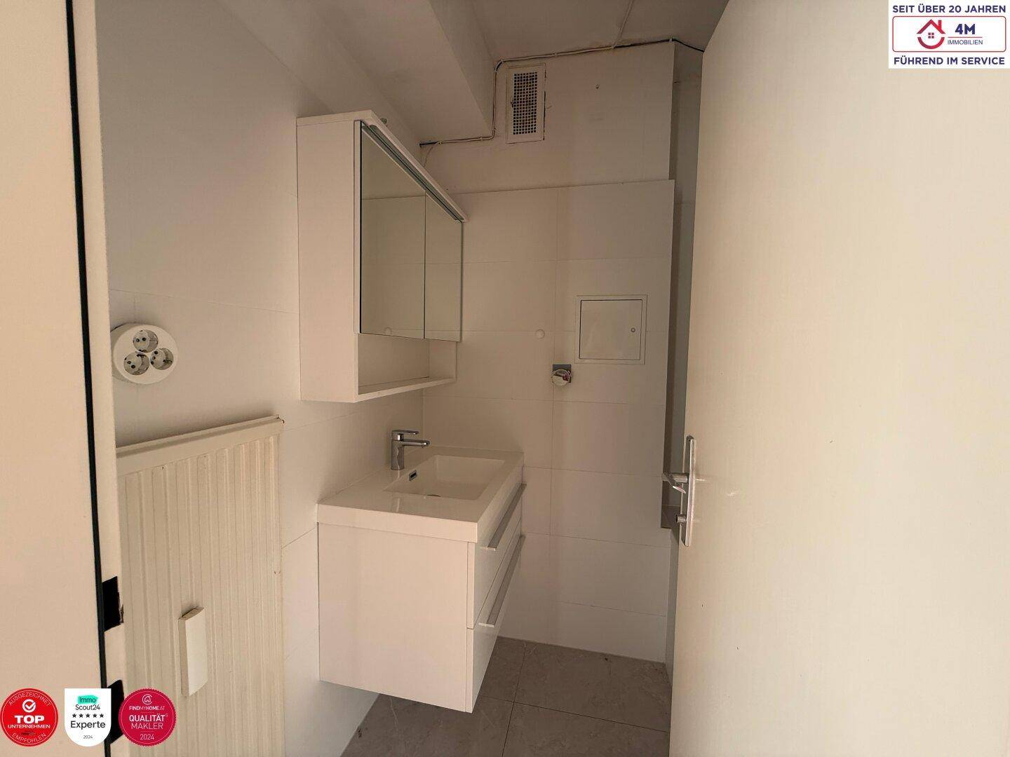 Modernes Badezimmer mit Waschtisch, Spiegelschrank und Heizkörper, in hellen Farben gehalten.