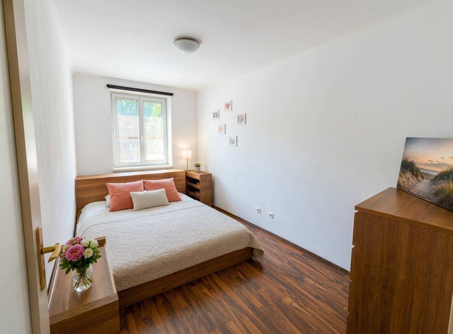 Gemütliches Schlafzimmer mit Holzbett, Nachttisch und Fenster mit Blick ins Grüne.
