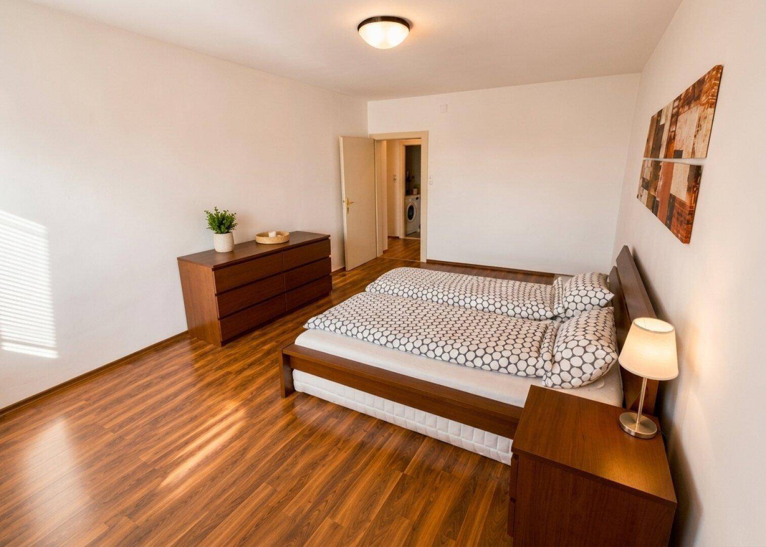 Schlafzimmer mit zwei Einzelbetten, Kommode und Zugang zu einem Nebenraum.