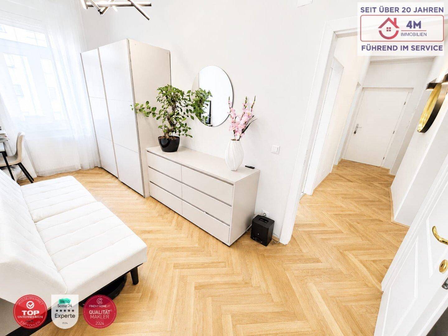 Helles Schlafzimmer mit Fischgrätparkett, weißer Kommode und Tagesbett.