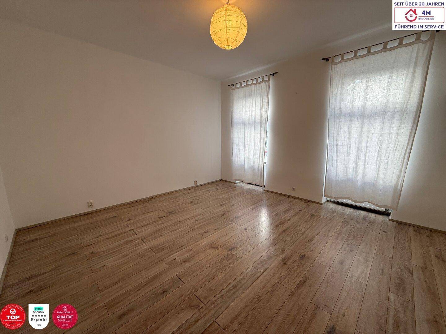 Geräumiges Zimmer mit hellem Holzfußboden und großen Fenstern für viel Tageslicht.