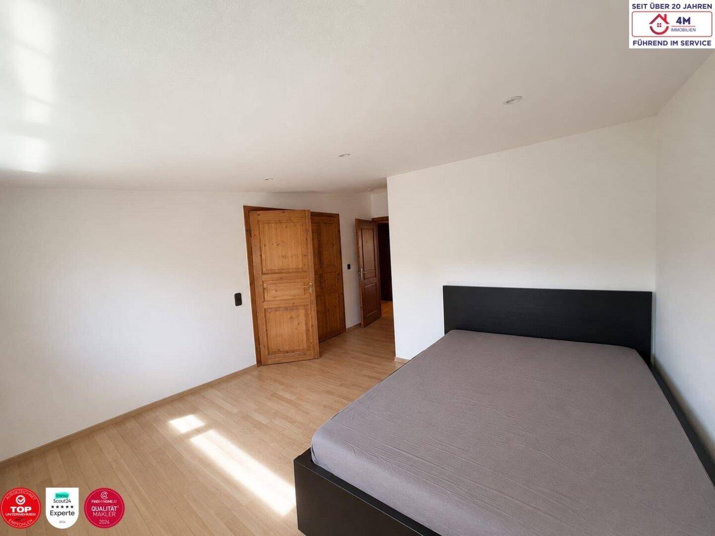 Helles Schlafzimmer mit weiß gestrichenen Wänden, Holzboden und einer modernen Bettkonstruktion, die viel Platz bietet.