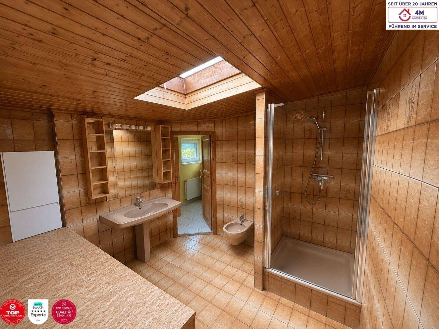 Badezimmer mit braunen Fliesen, Holzverkleidung, Dusche und Bidet, ergänzt durch ein Dachfenster für natürliches Licht.