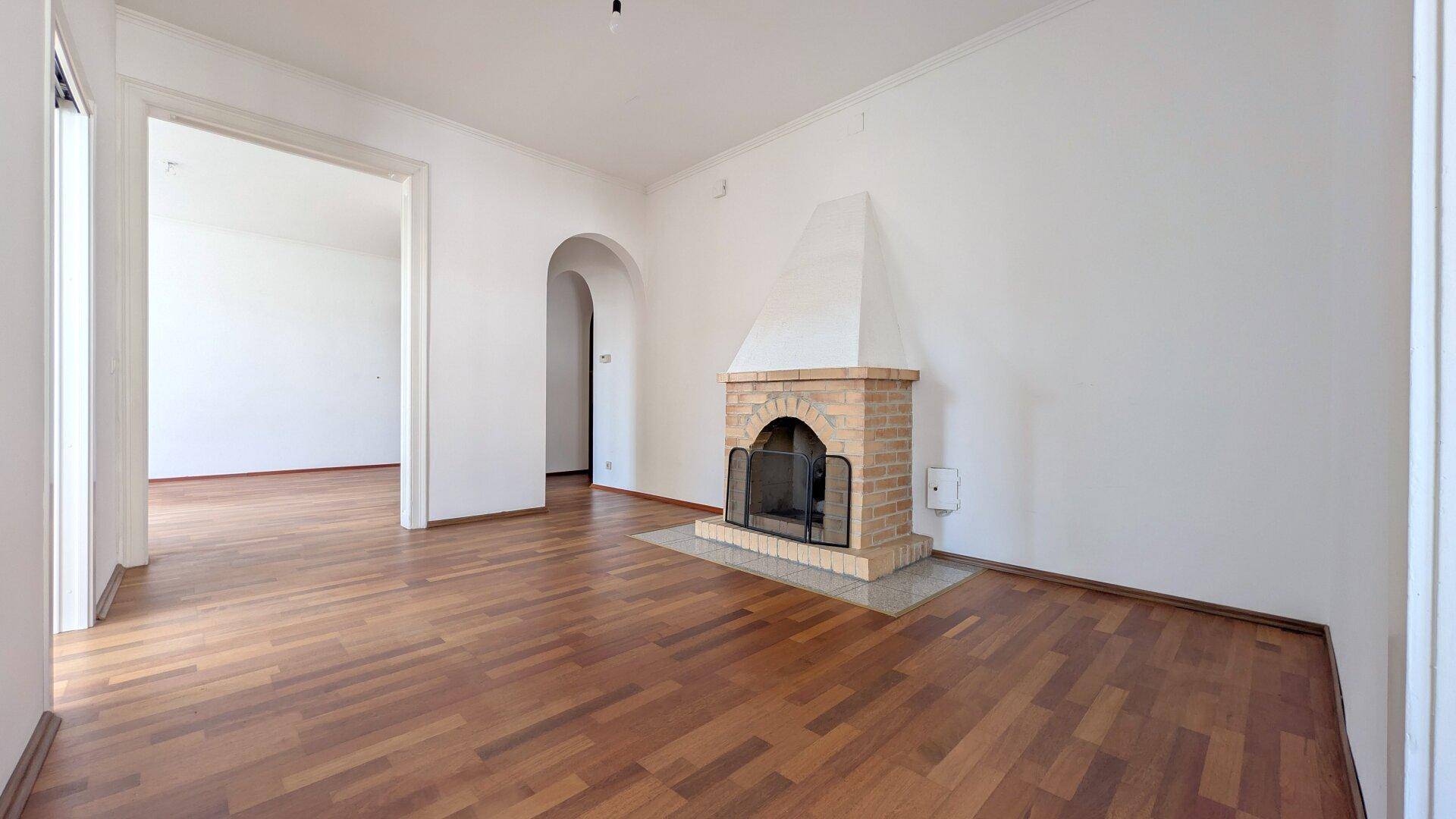 Geräumiges Wohnzimmer mit traditionellem Kamin aus Ziegeln und klassischem Parkettboden.