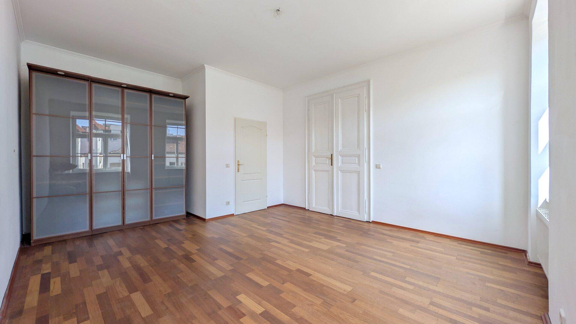 Schlafzimmer mit Parkettboden, einem großen Kleiderschrank mit Glastüren und weißen Flügeltüren.