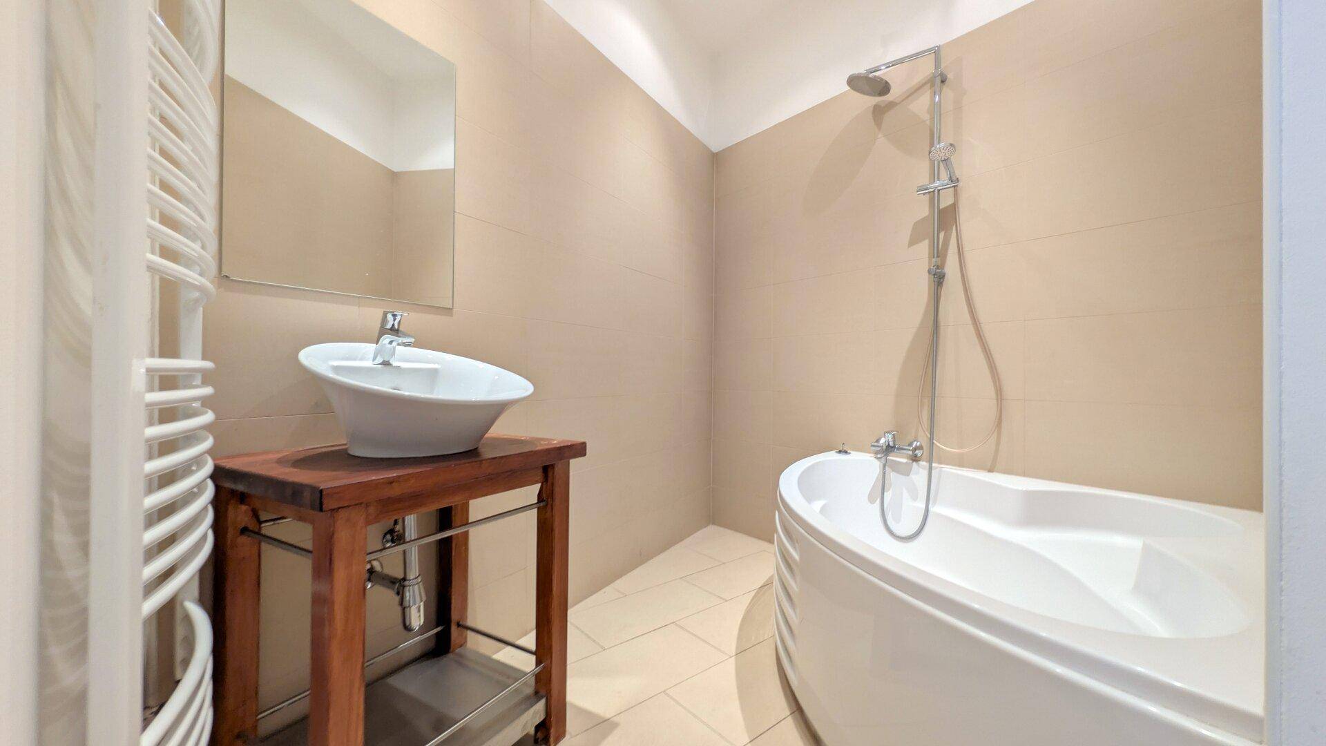 Modernes Badezimmer mit beigefarbenen Fliesen, Aufsatzwaschbecken und einer eleganten Badewanne.