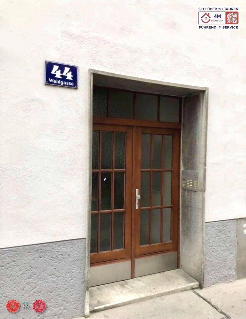 Eingangstür aus Holz mit Glasfeldern und Hausnummer an einer weißen Fassade.