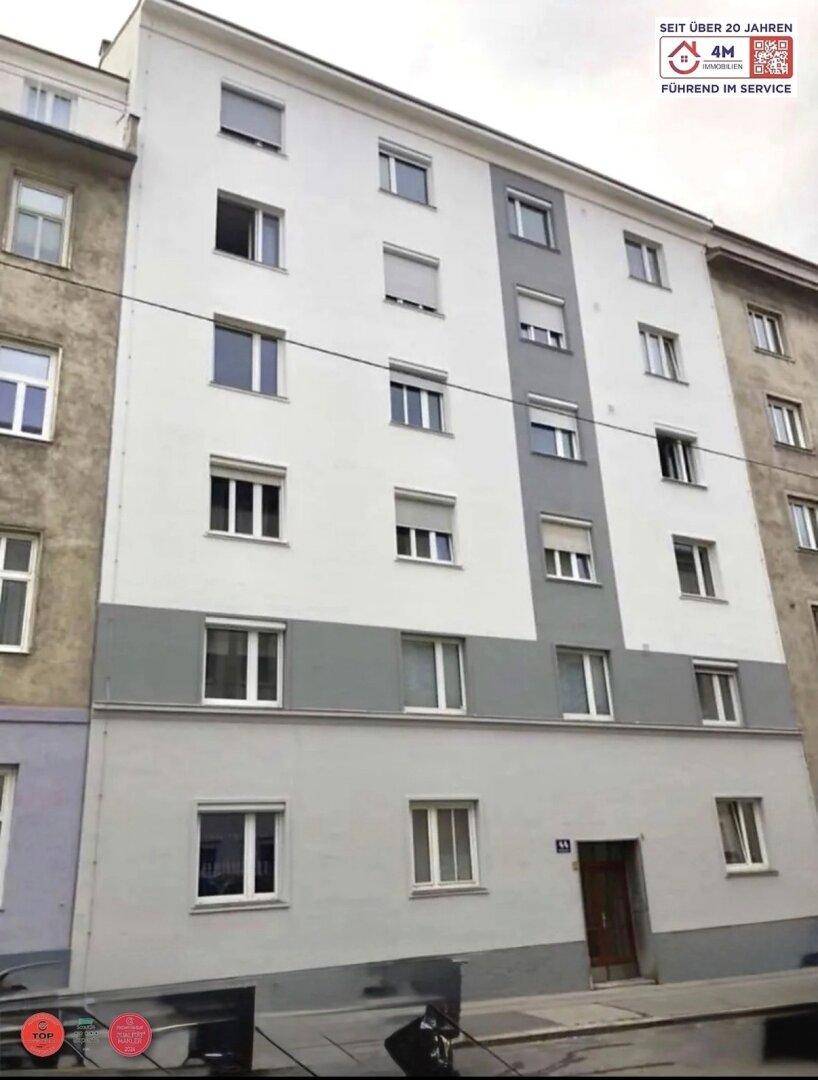 Mehrstöckiges Wohngebäude mit weiß-grauer Fassade und vielen Fenstern zur Straße hin.