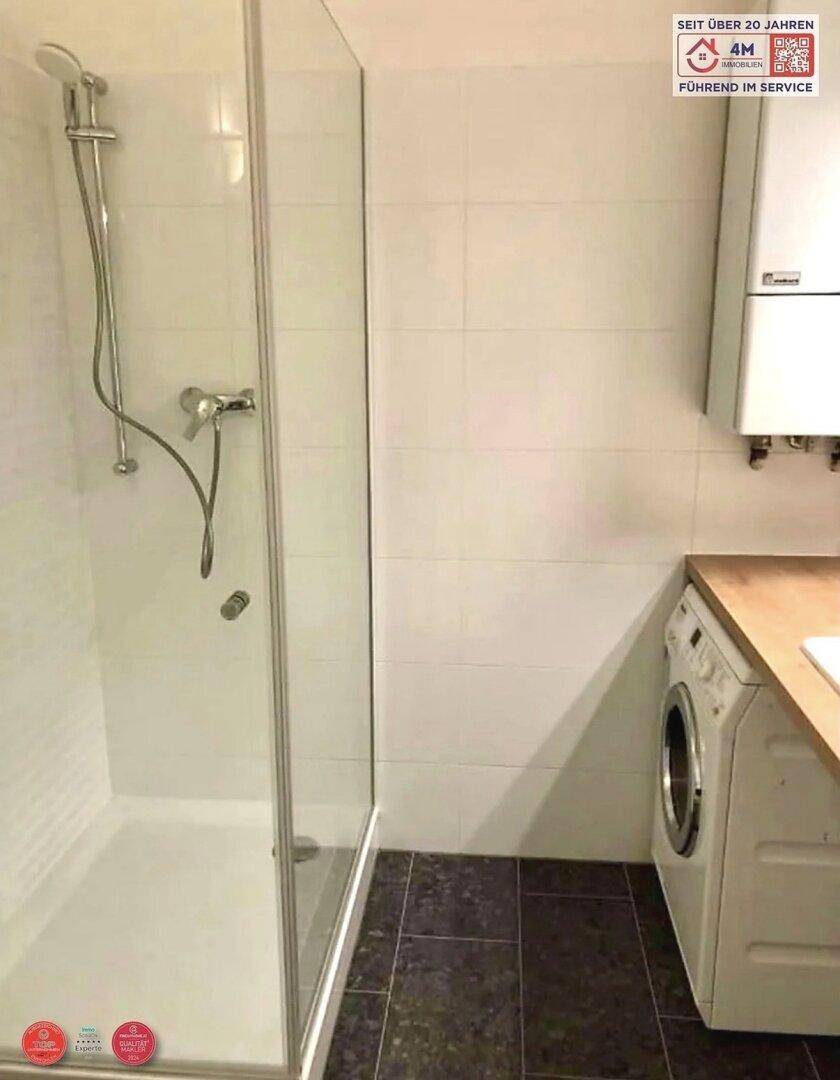 Modernes Badezimmer mit Duschkabine, Waschmaschine und Fliesenboden in dunklem Grau.