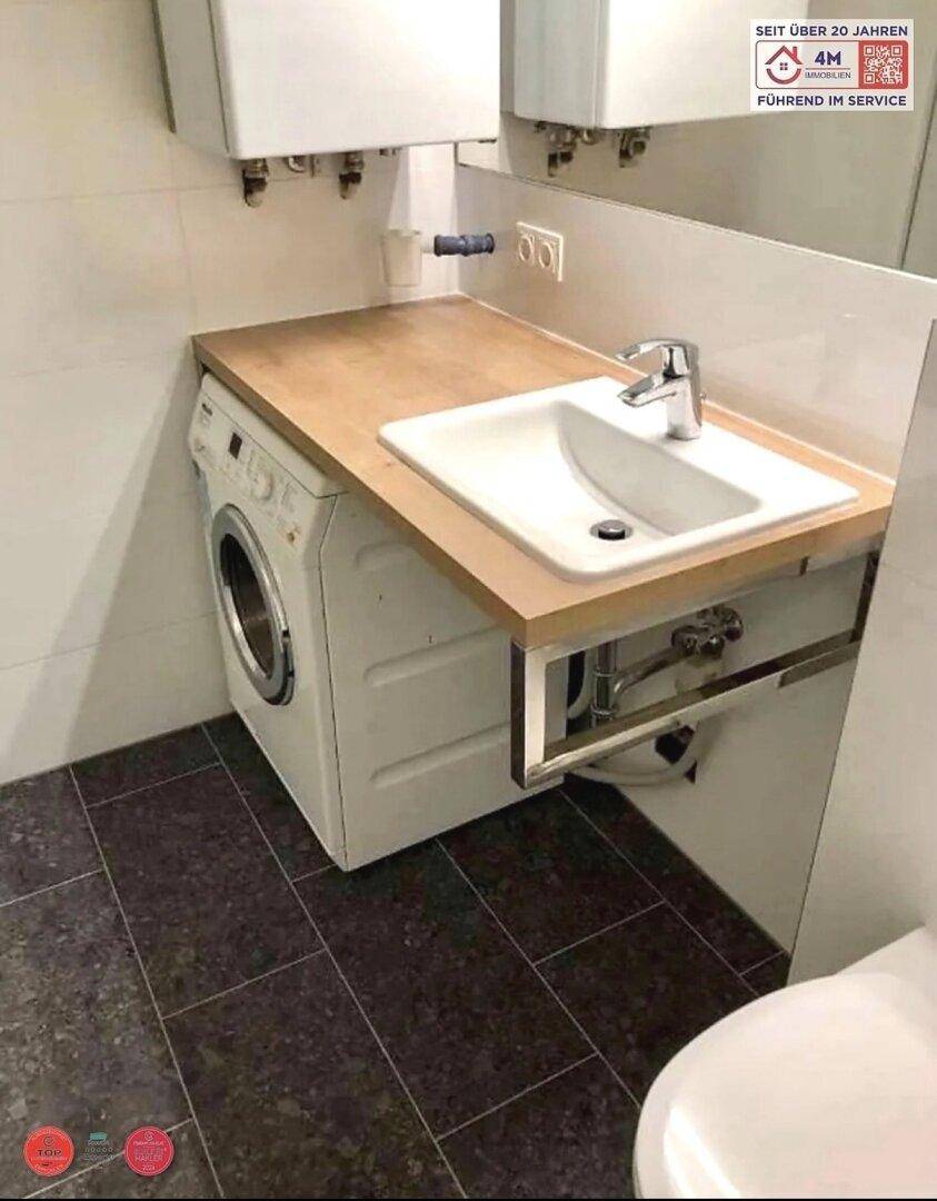 Badezimmer mit Waschbecken, Holzplatte und integrierter Waschmaschine unter dem Waschtisch.