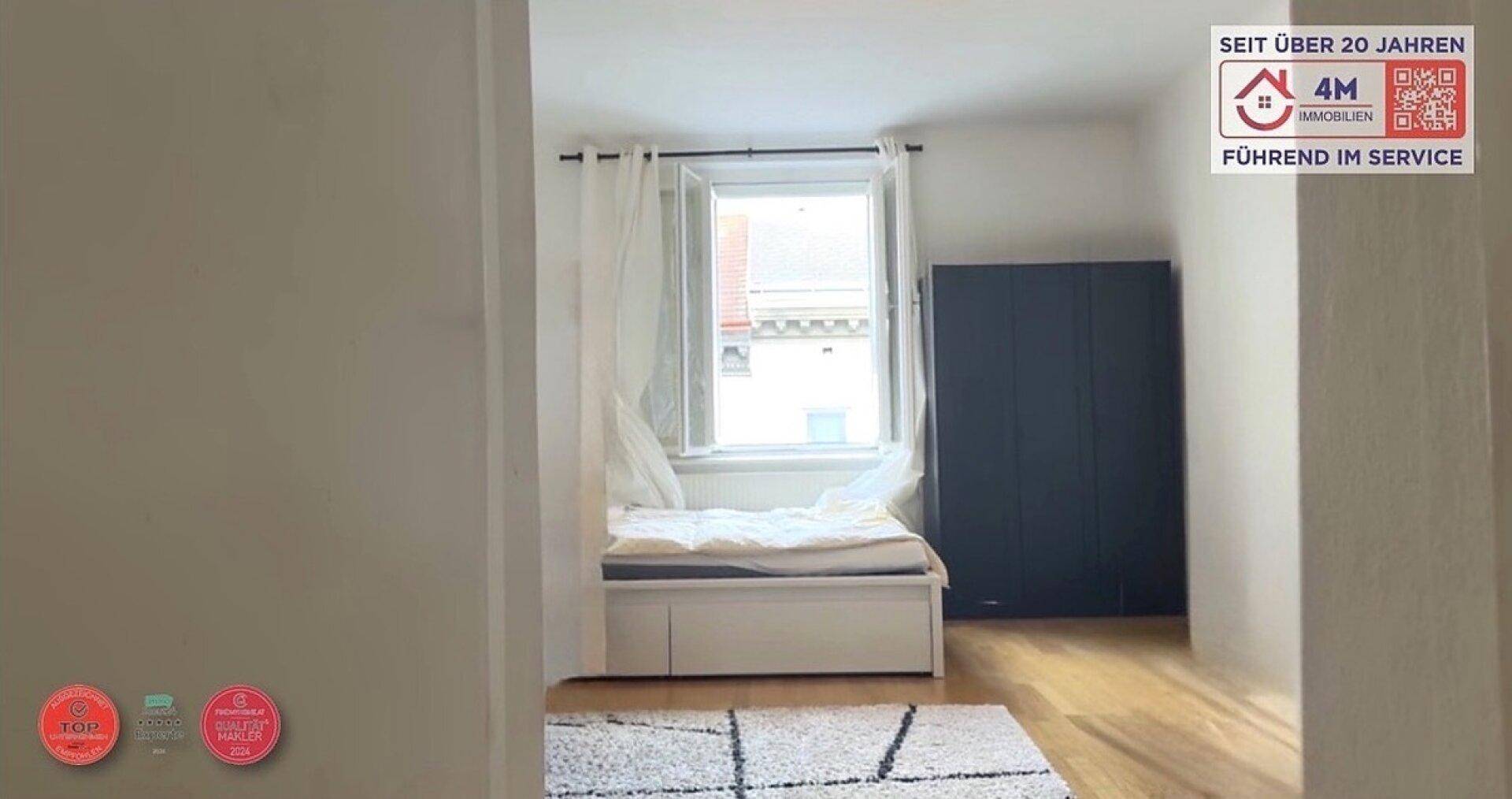 Schlafzimmer mit Einzelbett, dunklem Kleiderschrank und Fenster, das viel Tageslicht hereinlässt.