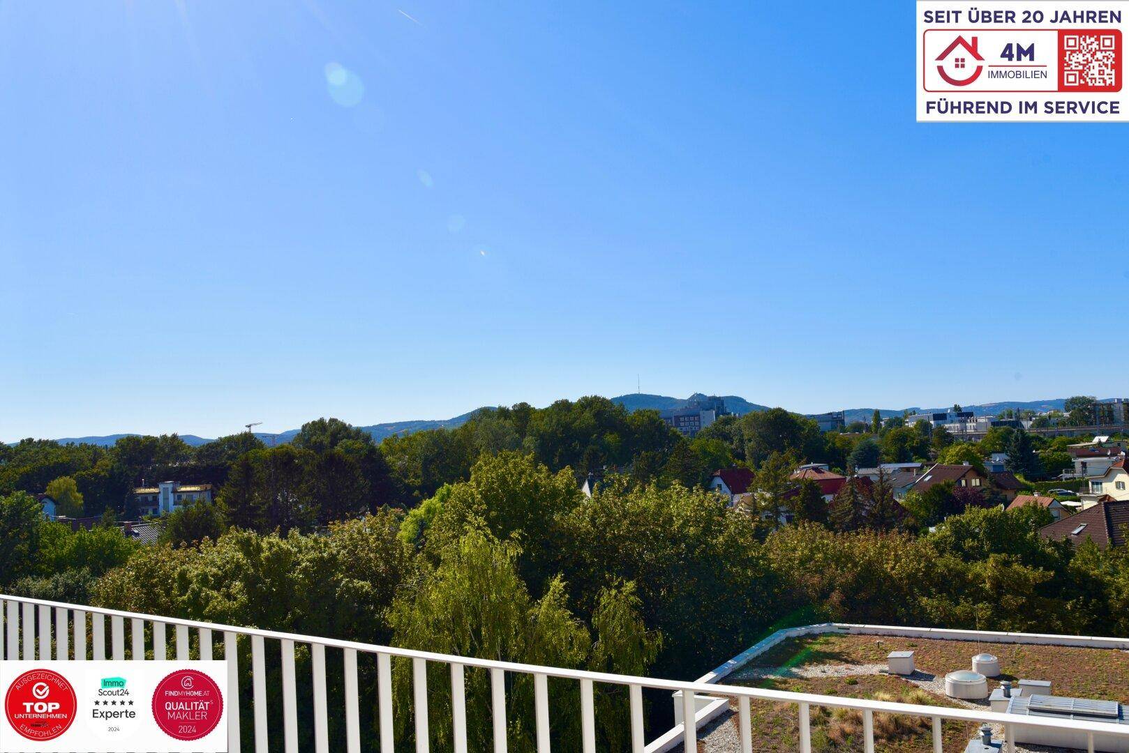 Weitläufiger Ausblick von einem Balkon über grüne Baumwipfel und eine hügelige Landschaft.
