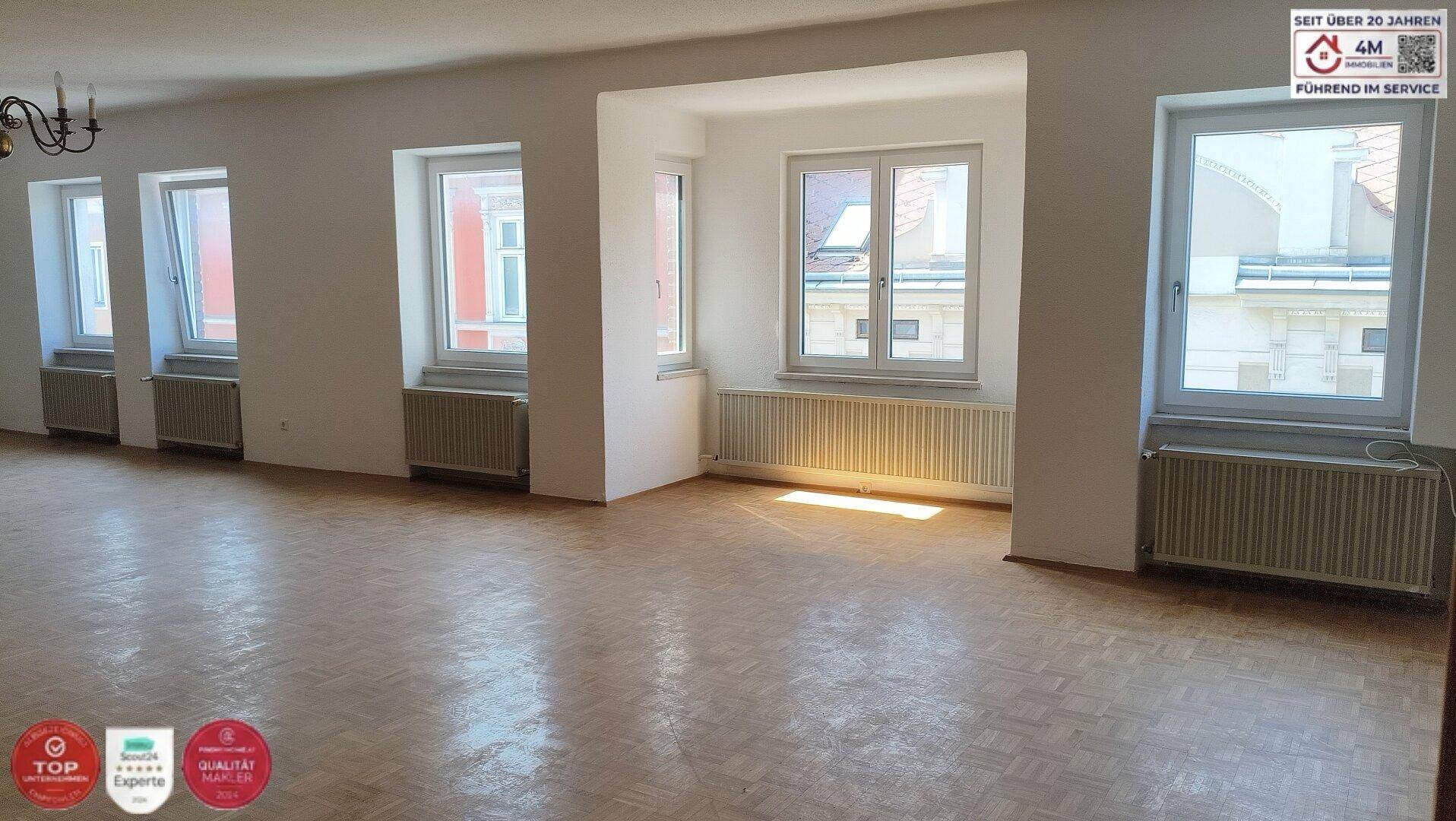 Geräumiges, helles Wohnzimmer mit Fischgrätparkettboden und mehreren Fenstern.