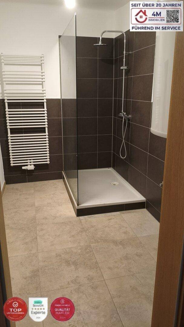 Modernes Badezimmer mit ebenerdiger Dusche, dunklen Wandfliesen und Handtuchheizkörper.