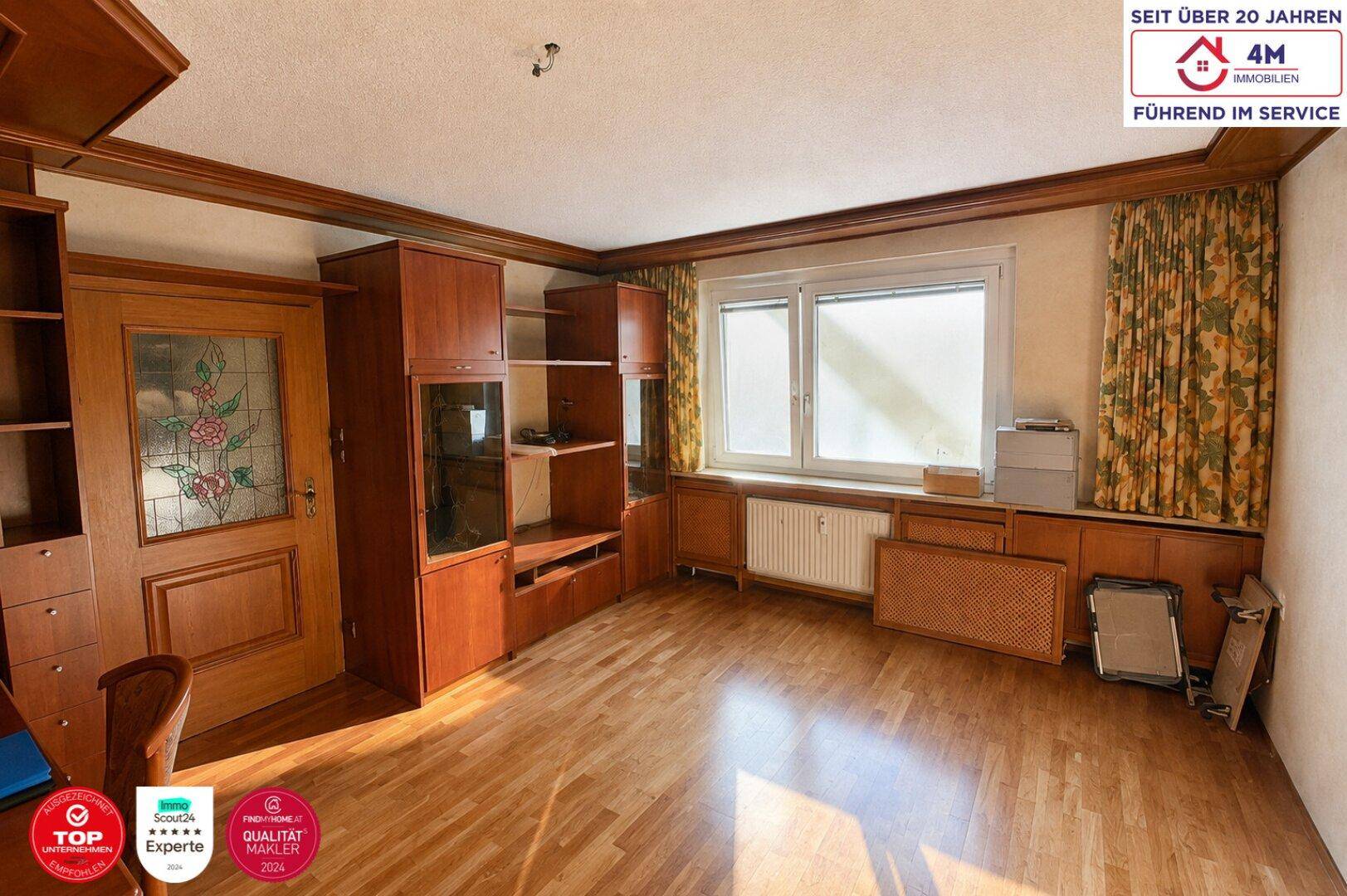 Wohnzimmer mit Holzeinbauten, Parkettboden und großem Fenster mit Blick nach draußen.