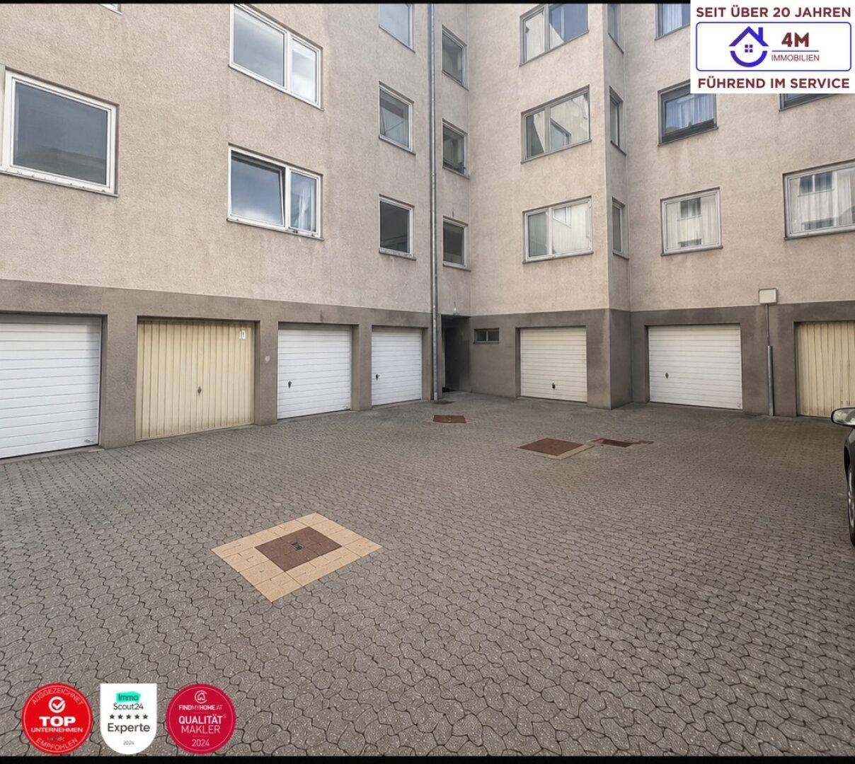 Hinterhofbereich eines Mehrfamilienhauses mit Garagen und gepflastertem Parkplatz.