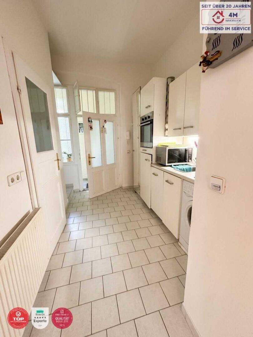 Schmale Küche mit weißen Einbauschränken, Fliesenboden und integrierter Waschmaschine.